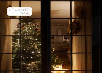 Albero di Natale illuminato visto attraverso una finestra, con luci calde e decorazioni che creano un’atmosfera natalizia in casa.